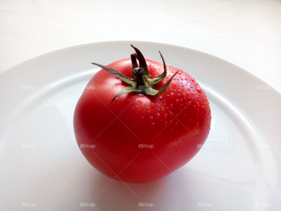 fresh red tomato with drops of water on the white plate