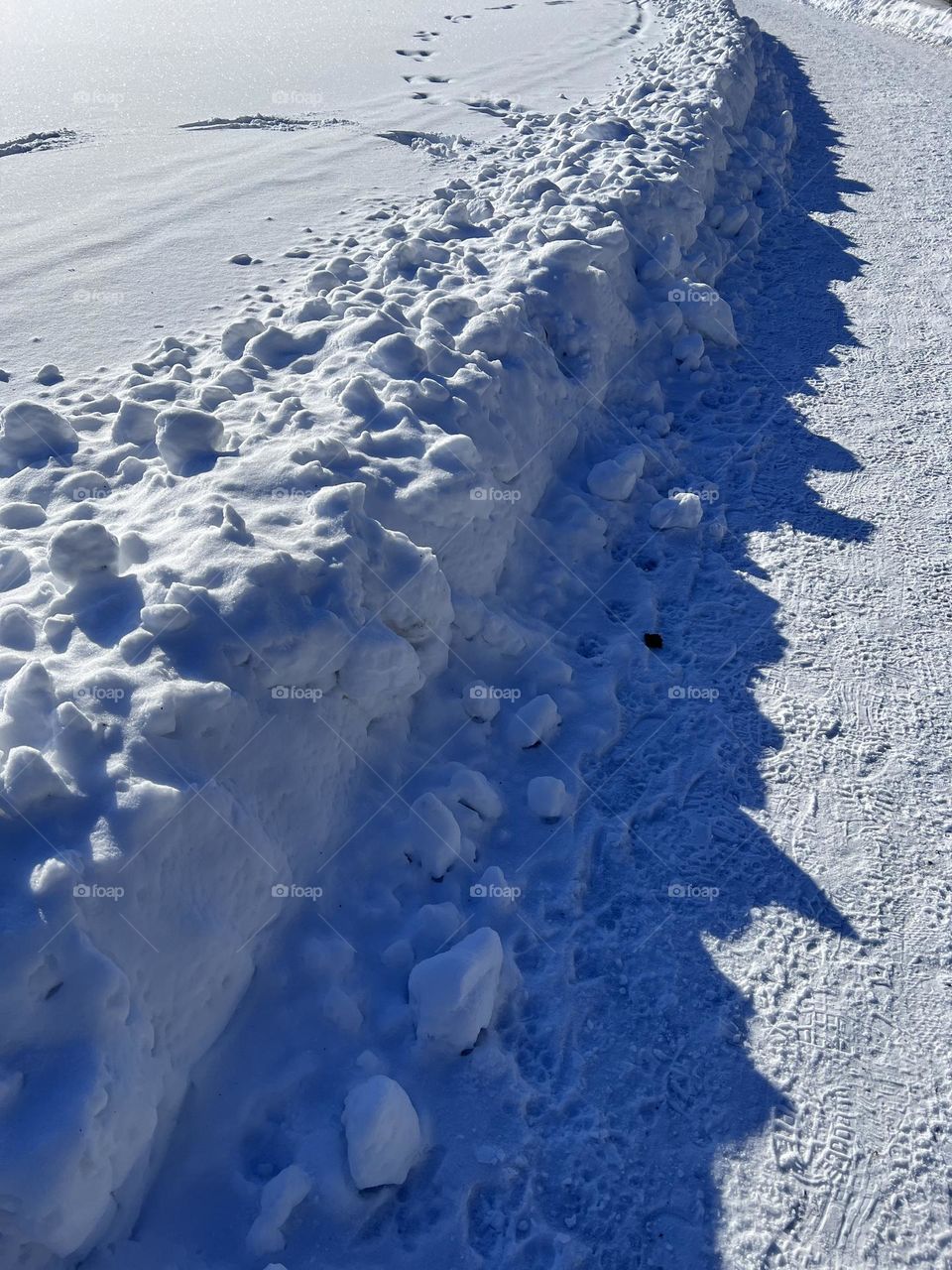 Bright white snow bank with the shadow on the footpath side