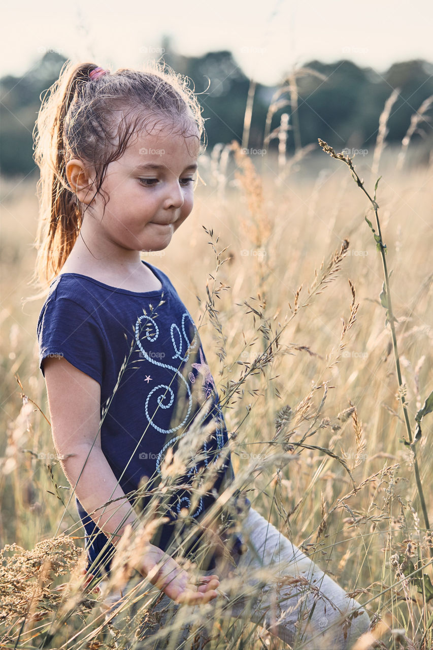 Little happy smiling girl playing in a tall grass in the countryside. Candid people, real moments, authentic situations