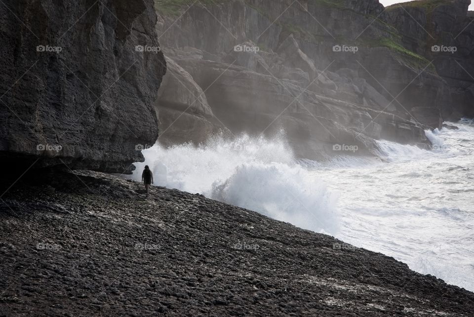 A person walks by the sea and the waves hit and splash 