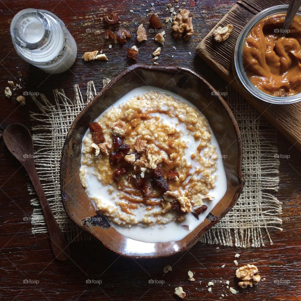 Pumpkin spiced oatmeal with homemade almond milk and crushed walnuts in a bowl on rustic wood table.