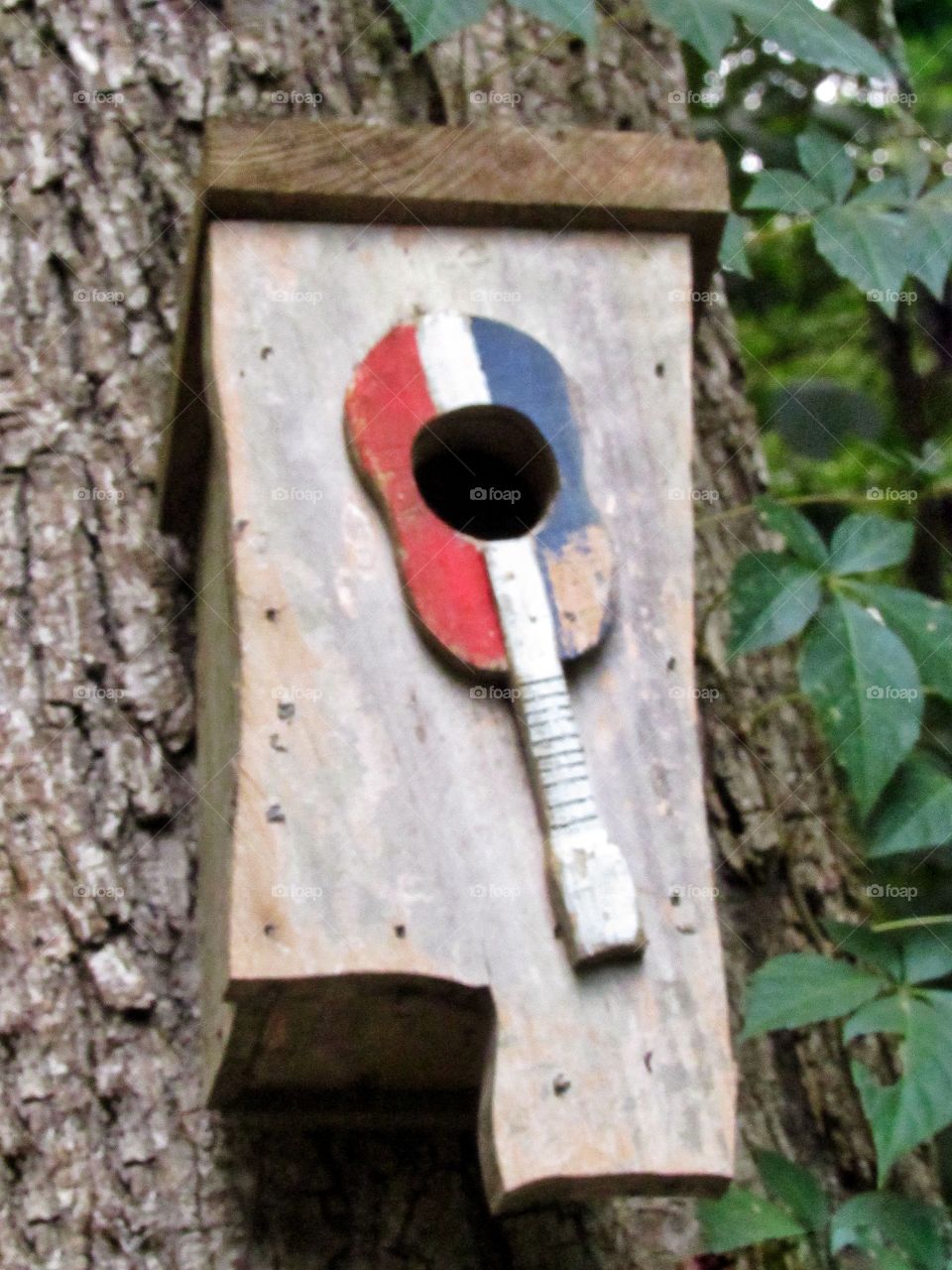wooden bird house in shape of Mississippi with red, white and blue guitar on front hanging on tree