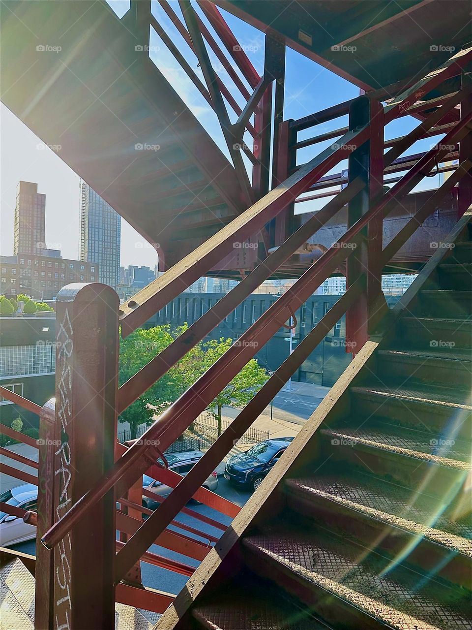 The red metal stairs of the “Pulaski Bridge” at “Newtown Creek” in “Greenpoint”, Bklyn have strong geometry. When the angled railings w four parallel bars overlap they create intrinsic patterns especially in light and dark. 2024. Hypnotic Productions