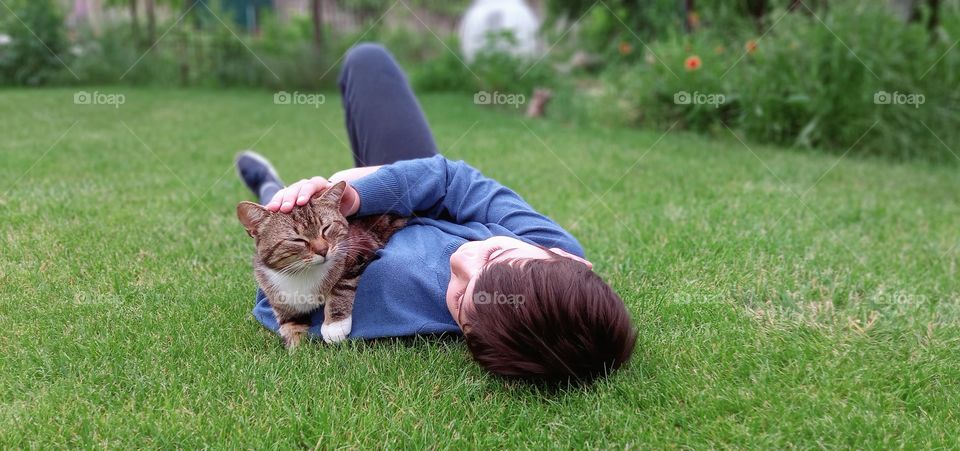 the boy lies on the grass and strokes the cat