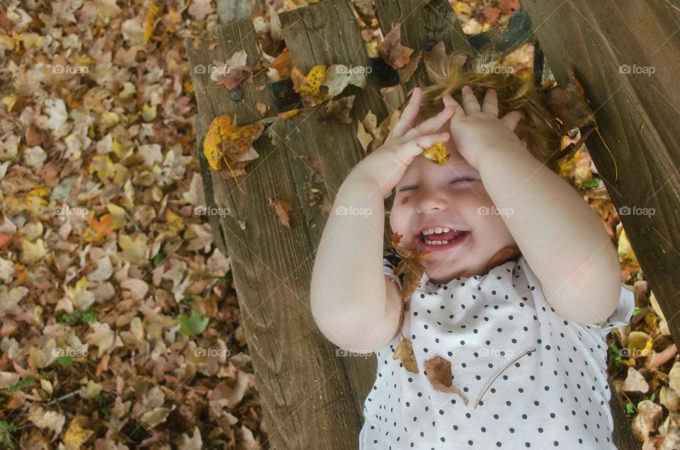 A little kid lying on bench in autumn