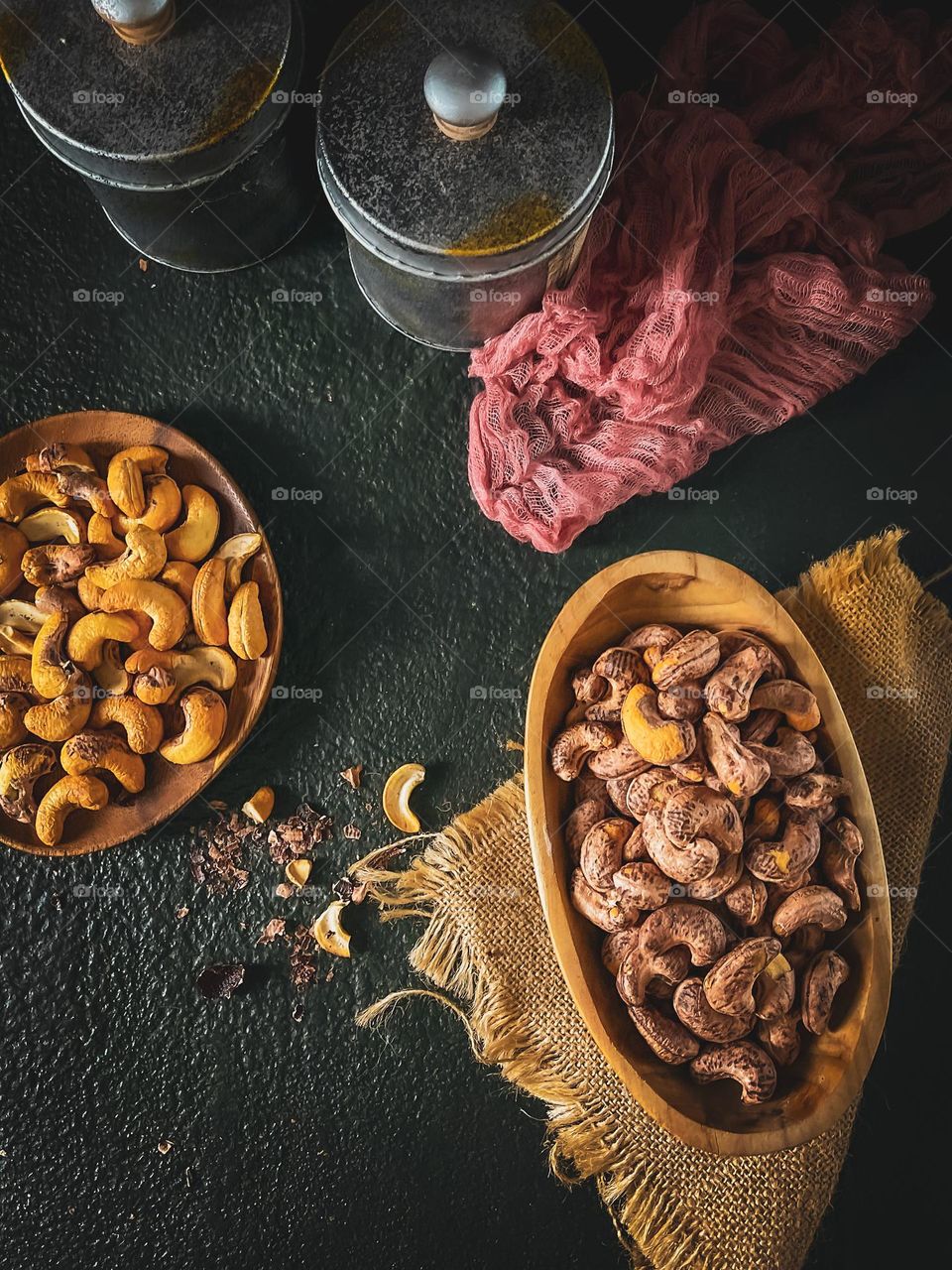 Cashew nuts in a wooden bowl and plate and some canisters beside it