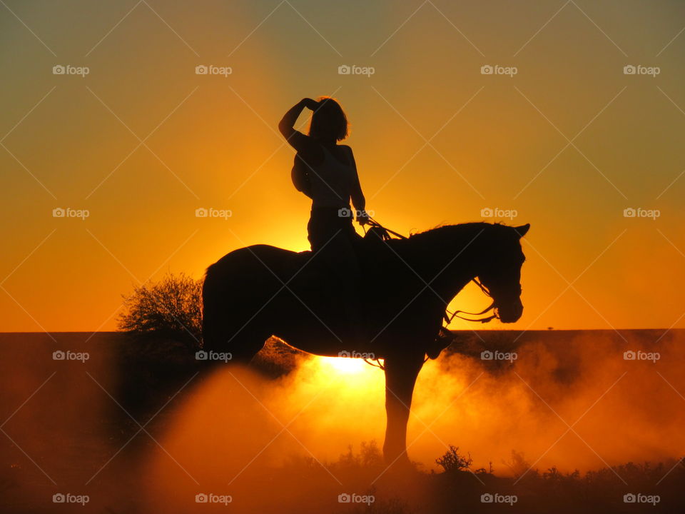 Young woman sitting on her horse, she enjoys the last sunbeams before nightfall. Looking as far a she can. while the dust comes to rest after a sudden stop. Oh Africa with you golden sunsets!