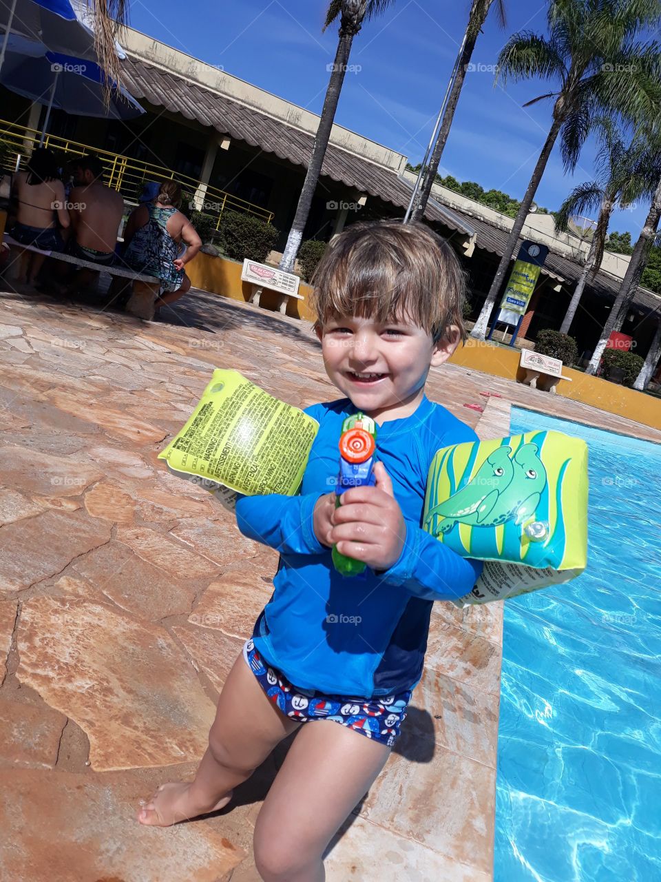 child playing with nerf in the pool with buoys in his arms