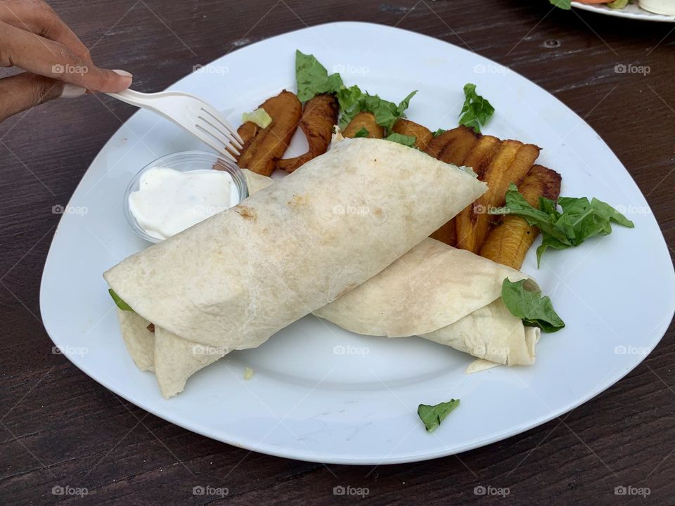 Chicken curry wrap and a person ready to eat sweet bananas on a white serving plate. 