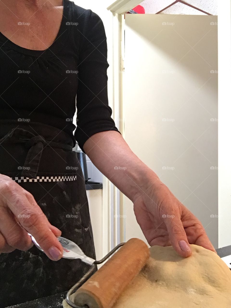 Handy woman in the kitchen working with bread dough for pita and wearing black apron 