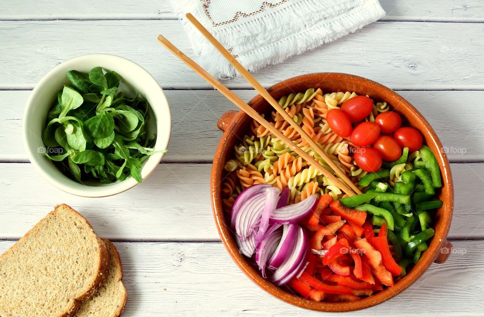 Pasta ingredients and bowl of basil on table