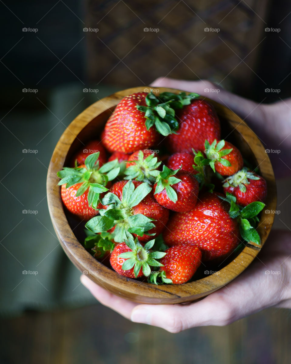 A human hand holding bowl of strawberries