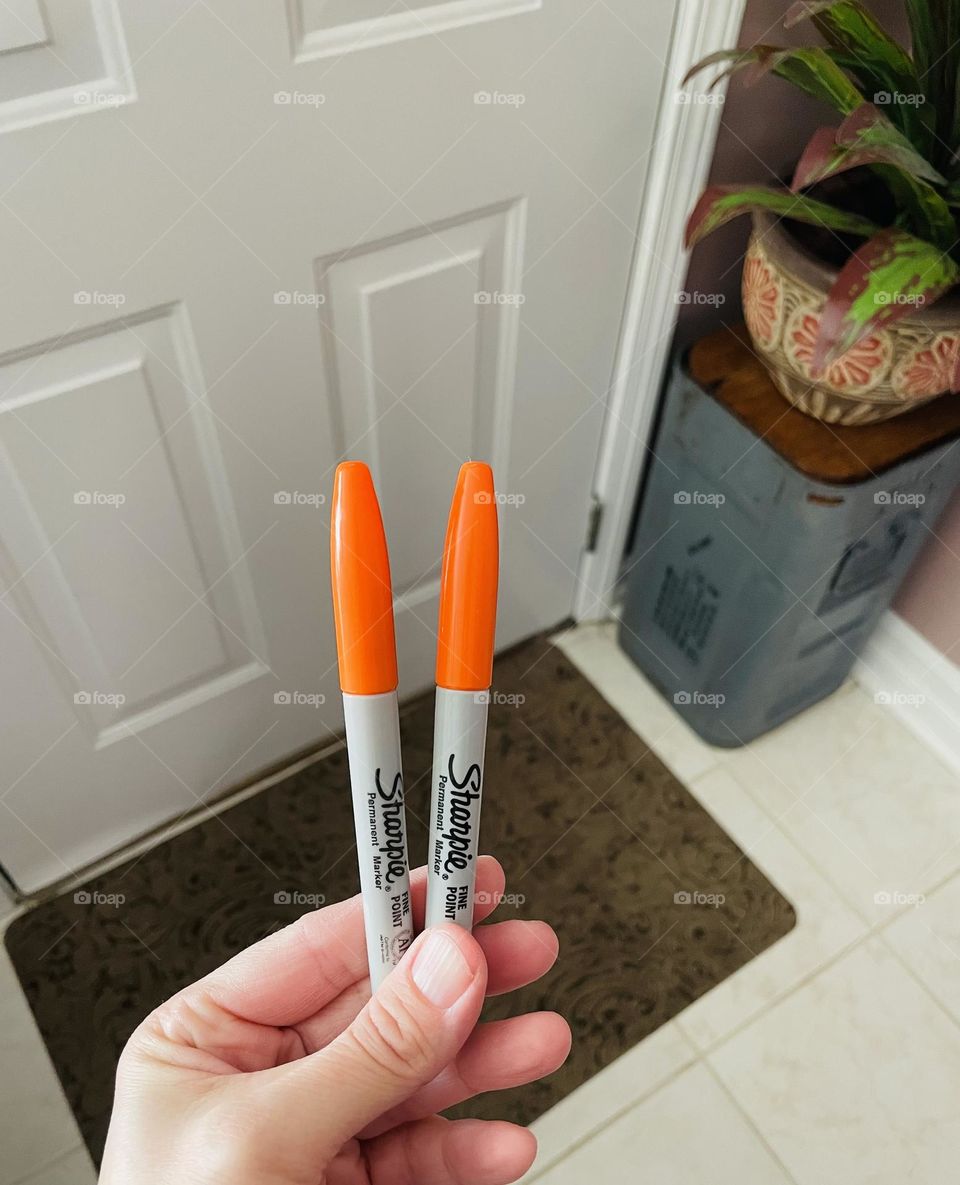 Woman’s hand holding Sharpie markers, orange markers for the holidays, permanent markers being held by hand, hand holding art supplies