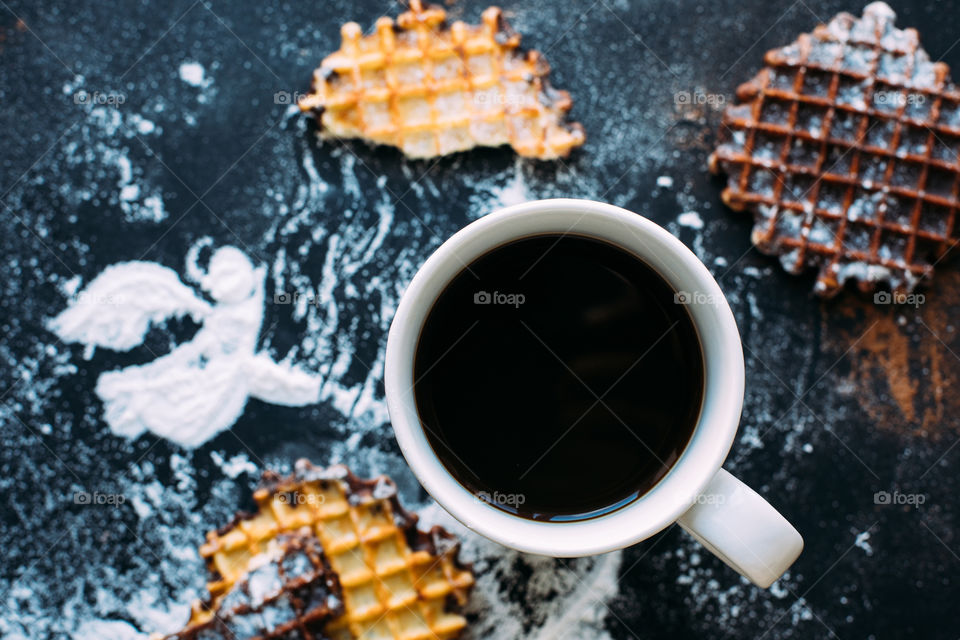 Cup of coffee with Belgian waffles on dark background with snow angel