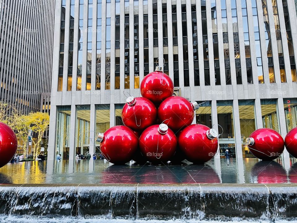 Red Ornaments  - Giant  red Christmas tree ornament balls sits on top of the water fountain outside an office tower on the Avenue of the Americas. 