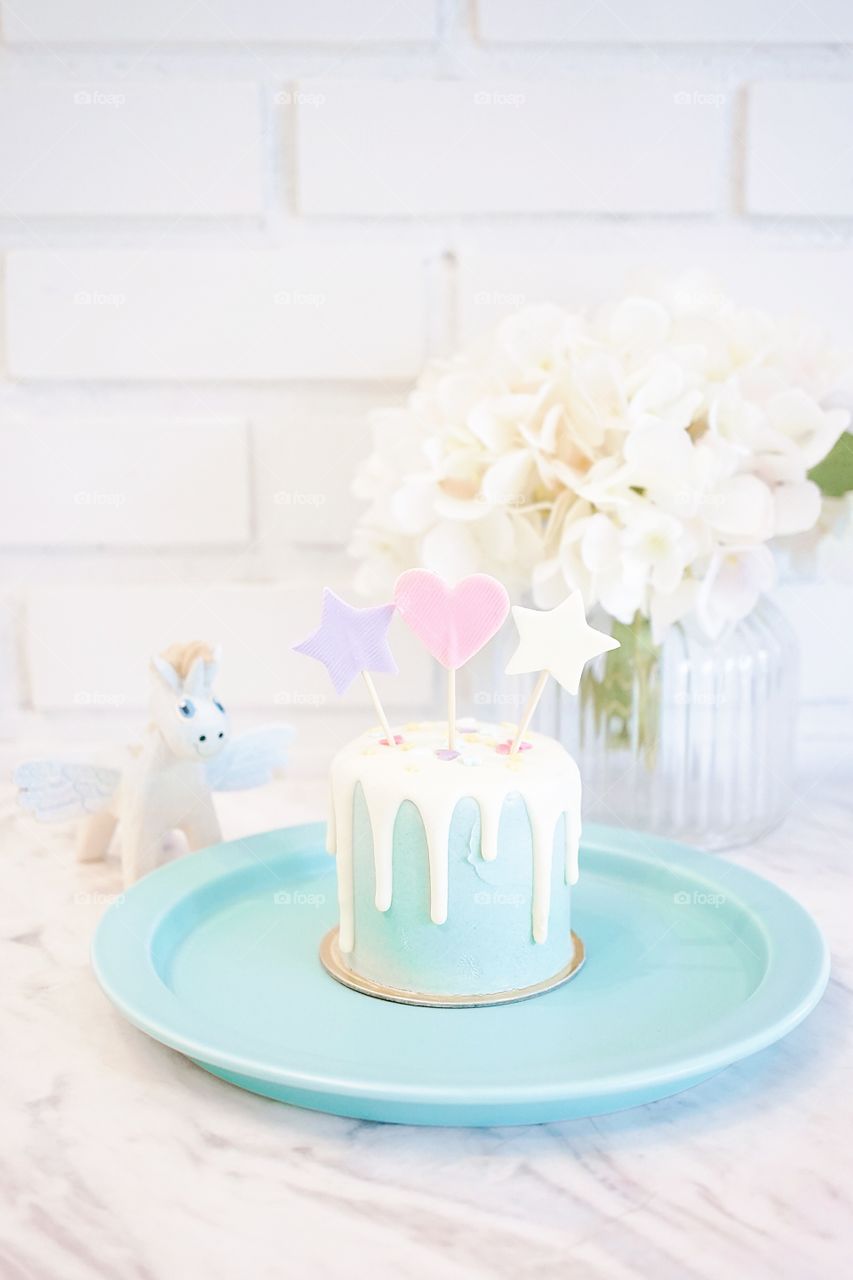 Birthday cake with stars and a pink heart cake decor. An unicorn stands in the background. Sweet and dreamy concept