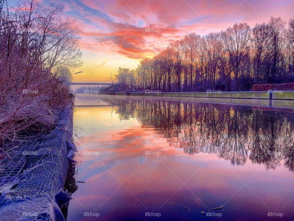Colorful and dramatic sunrise or sunset over a winter forest landscape with a river running through it which reflects the colorful clouds and sky