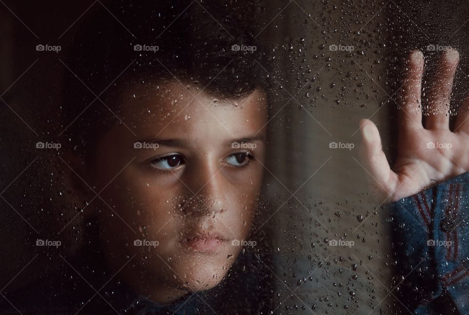 Close up portrait shot of my nephew watching at the window in rainy day