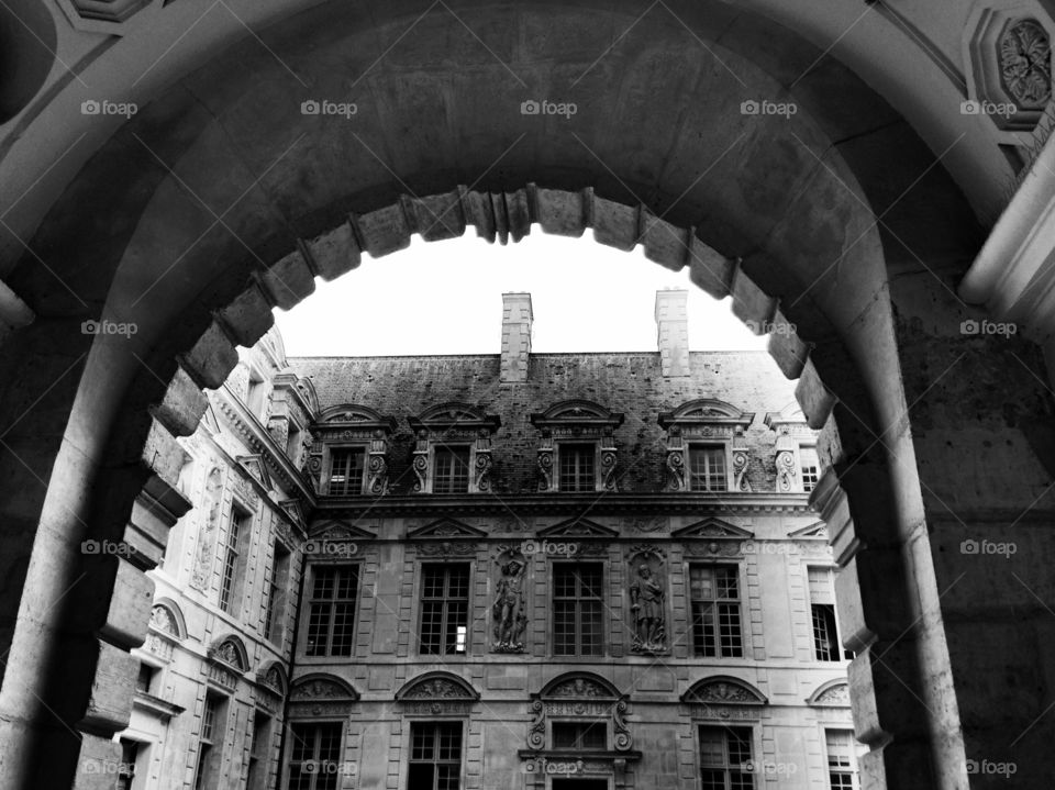 Arched walkway into courtyard. Buildings surround courtyard -- entry through large stone Arch. 