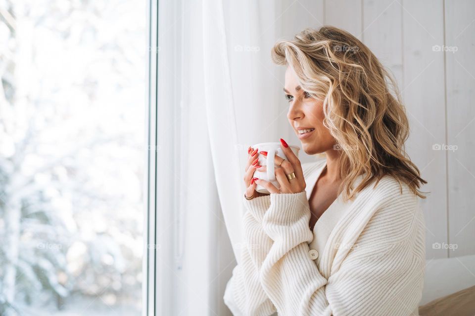 Beautiful woman with cup of hot drink at home in winter season 