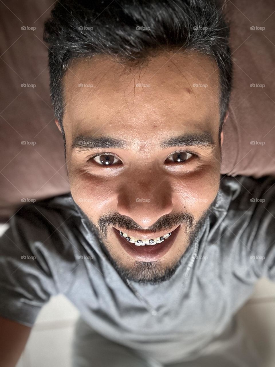 Man lying down on his bed while he looks to the camera and looking happy at his face.