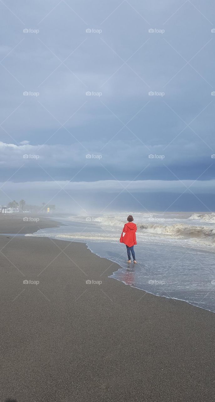 Woman on the seashore during a storm. Fog, clouds, waves and a girl in a red cloak is walking on the water.