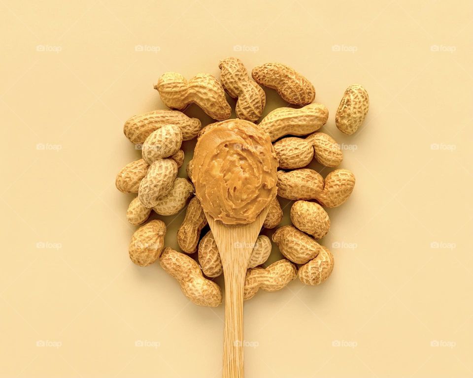Wooden spoon with peanut butter on beige background 
