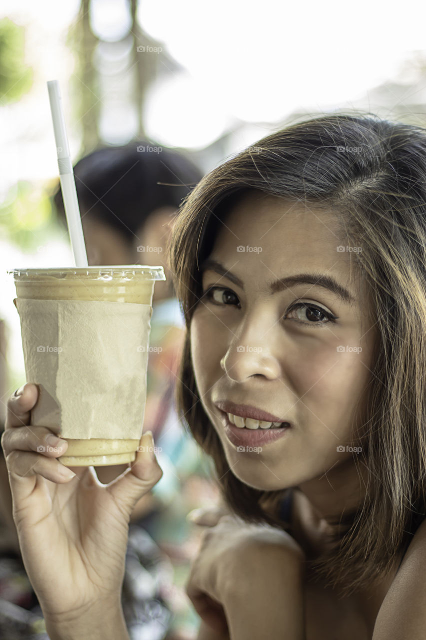 Asian woman holding glass of iced coffee.