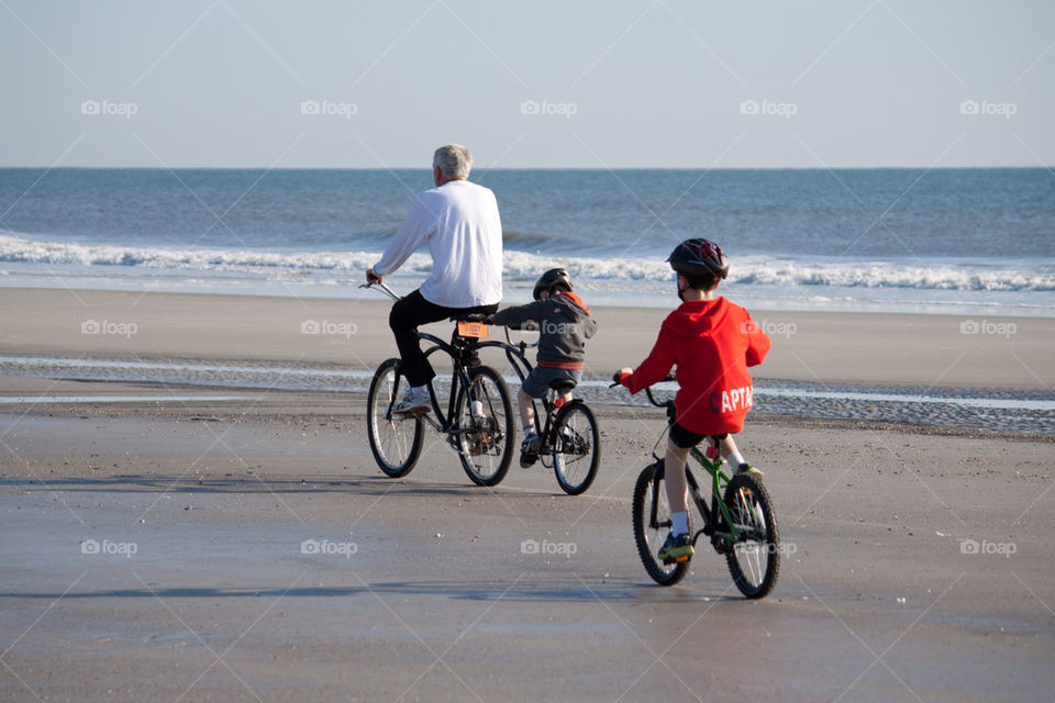 Father and sons riding bikes on the beach
