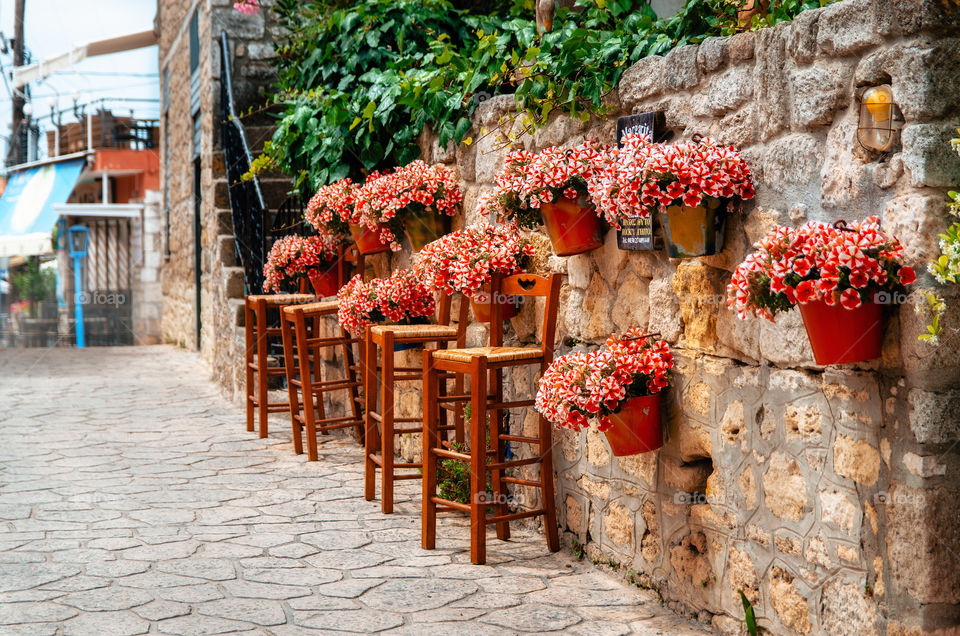 Pots of red flowers on a stone wall in full bloom with barstools around the cafe, Afitos, Halkidiki, Greece