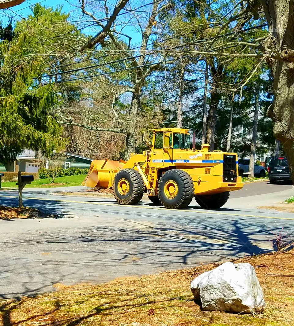 Front end loader heavy equipment. Bright yellow tractor driving on road in summer. Blue sky & sunshine day!