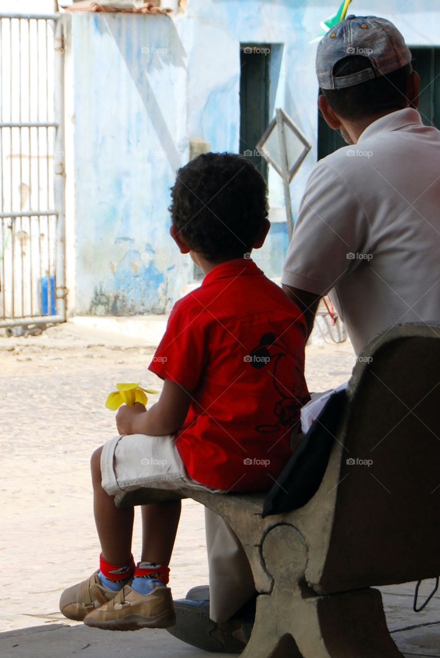A boy waiting someone at the bus stop with a yellow flower in his hand. (Brazil)
