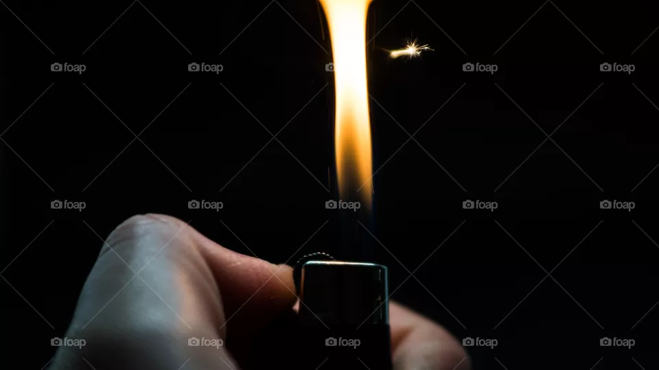 A person has lighters in his hands and he lights it through a flint wheel, the lighter ignites, sparks and fire appear, close-up on a black background.