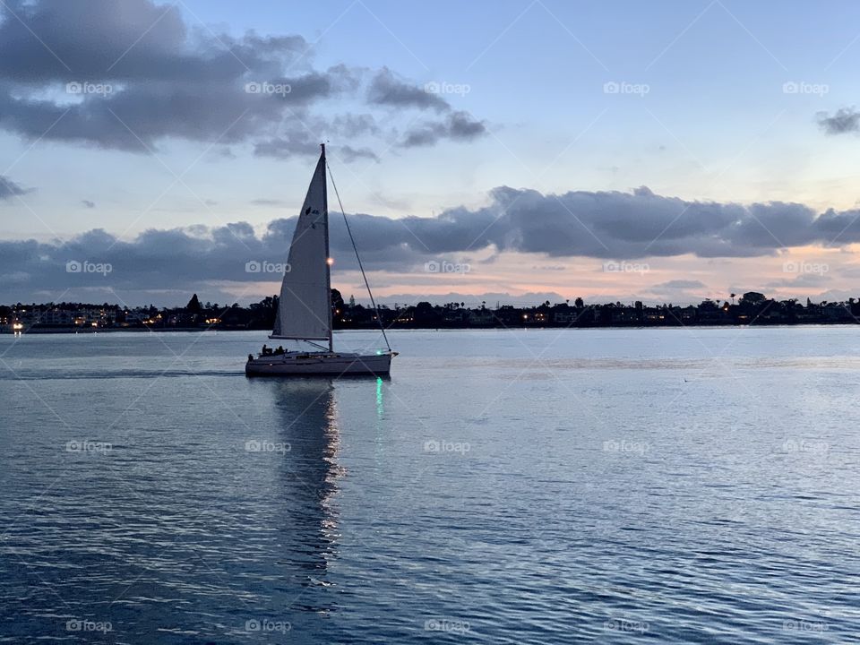 Sailboat sailing into a harbor during sunset.