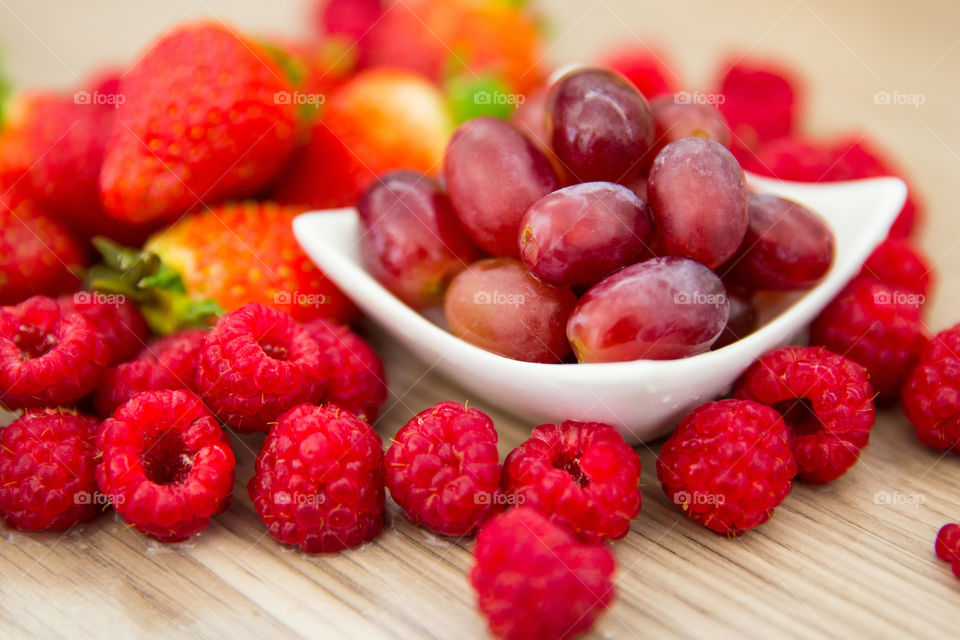 Fresh healthy red summer fruits and berries with grapes in a white dish, strawberries and raspberries. Fresh fruit on a wooden backdrop.