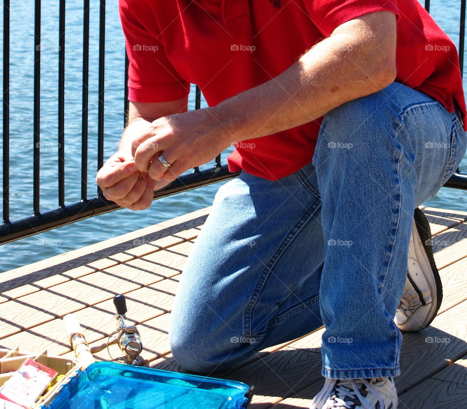 A fisherman on a dock rigs up his line. 