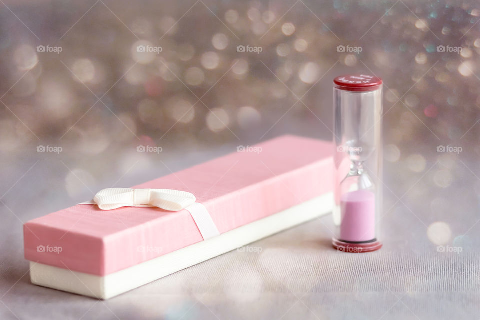 Festive still life of a pink gift box and an hourglass on a background with bokeh.