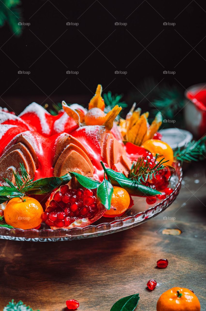 Christmas table setting. Bundt cake pudding sprinkled with sugar powder decorated with pomegranate and tangerines. High quality photo