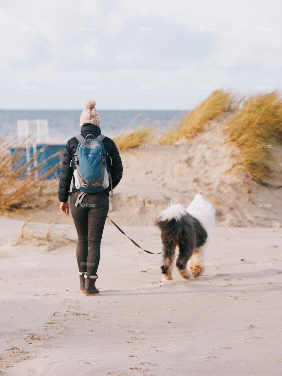 Young woman walking with big fluffy dog on seaside in autumn day