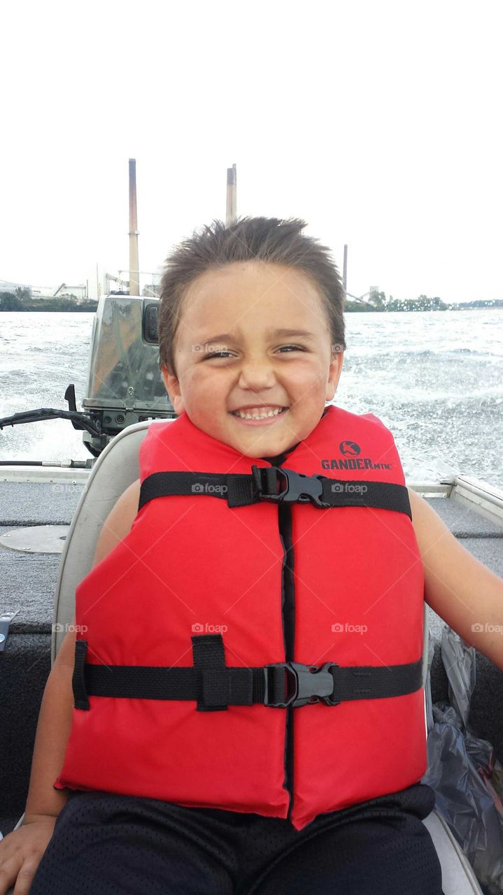 child smiling riding in a boat with life jacket on sl