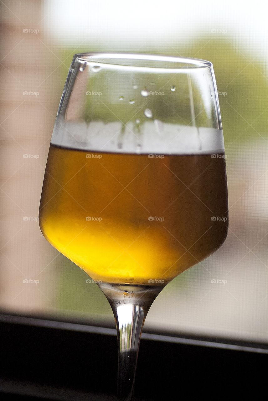A glass of beer sits on a window ledge.
