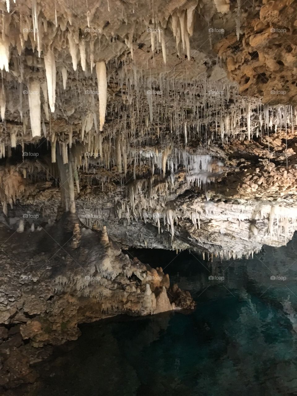 The colorless stalactites hang down from the calcium ceiling and contrast against the dark, crystal clear water below.