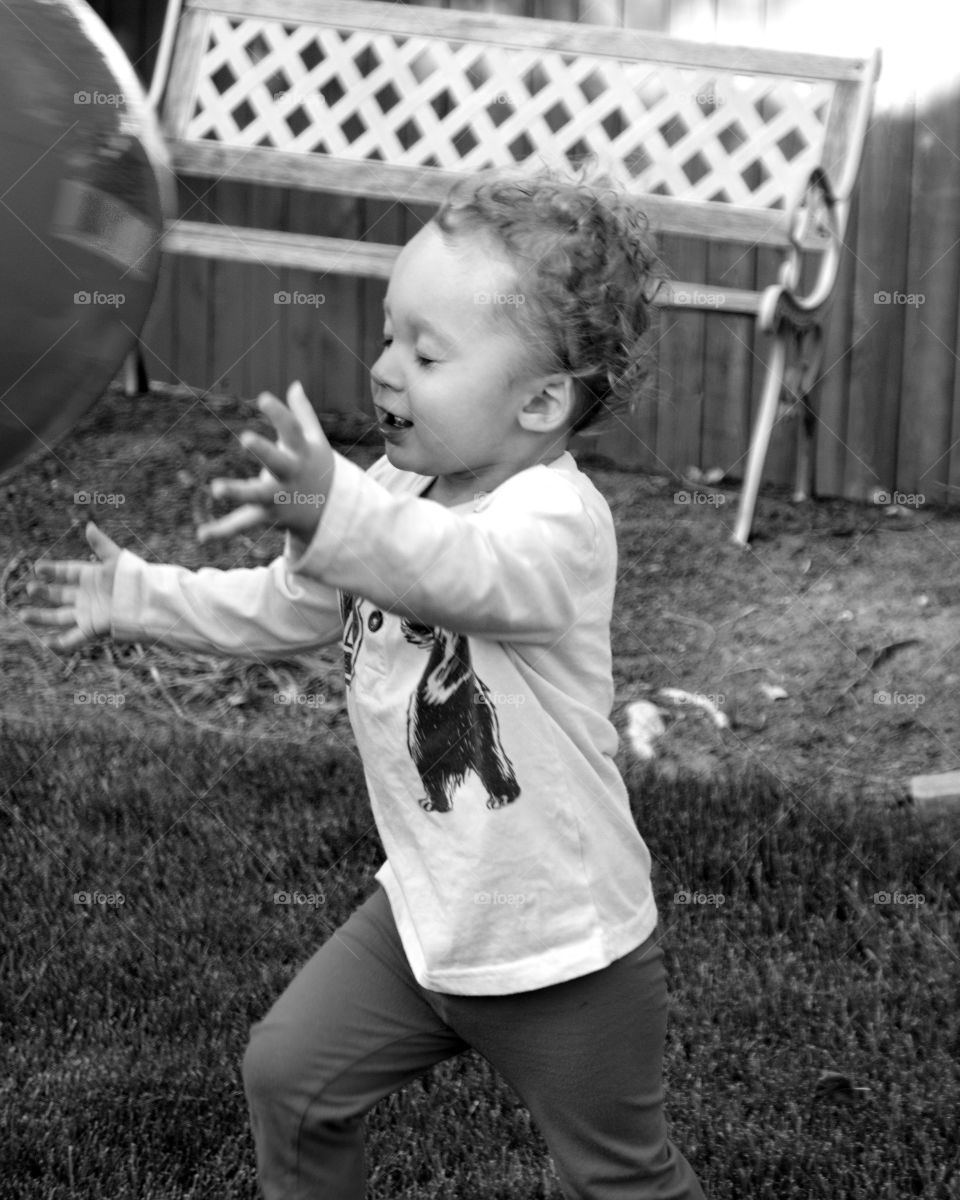 An adorable toddler boy plays catch with a huge ball in the yard on a sunny summer day. 