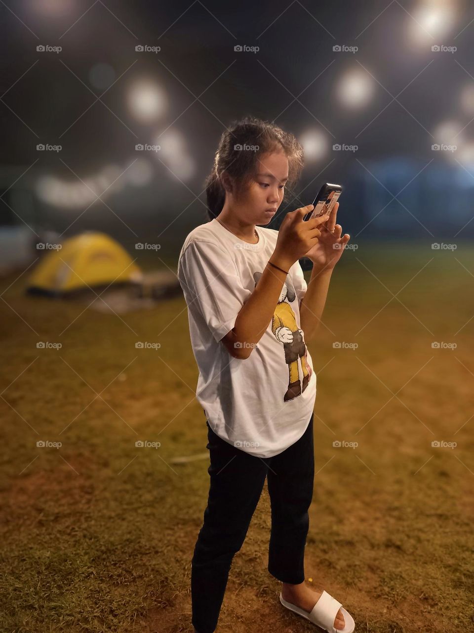 Portrait of a girl playing cellphone at night in the field.