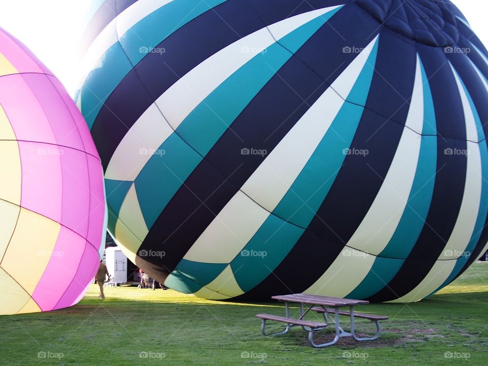 Two bright and colorful hot air balloons on the grass of Ochoco Park filling with helium for a morning flight over Prineville in Central Oregon on a beautiful summer morning as the sun rises.