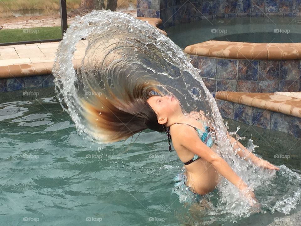 Small girl splashing hair in swimming pool