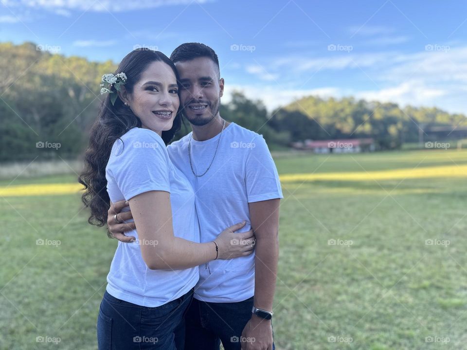 Young couple posing for a portrait on a beautiful and green landscape in a sunny day.