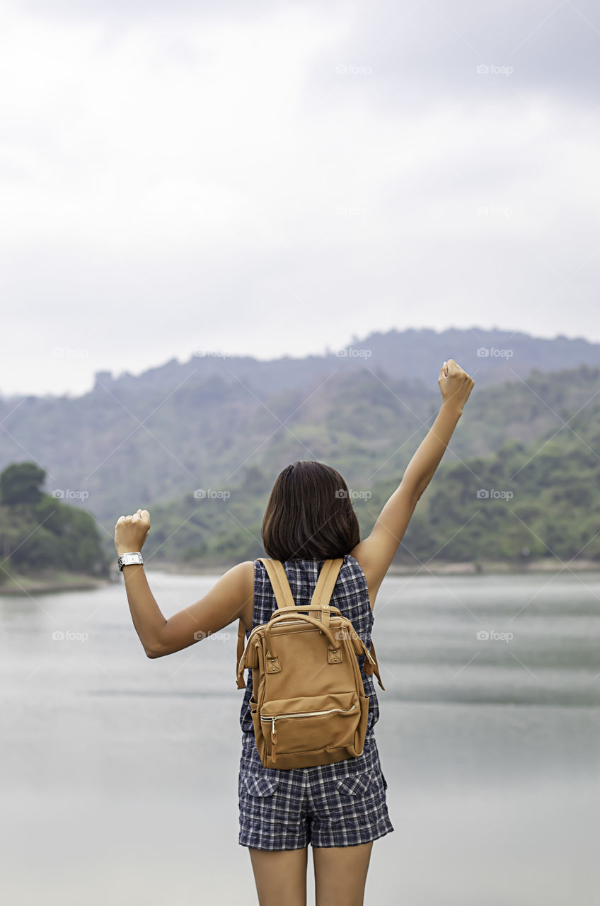 Women raise their arms and shoulder backpack Background mountains and water at Wang Bon dam ,Nakhon nayok in Thailand.