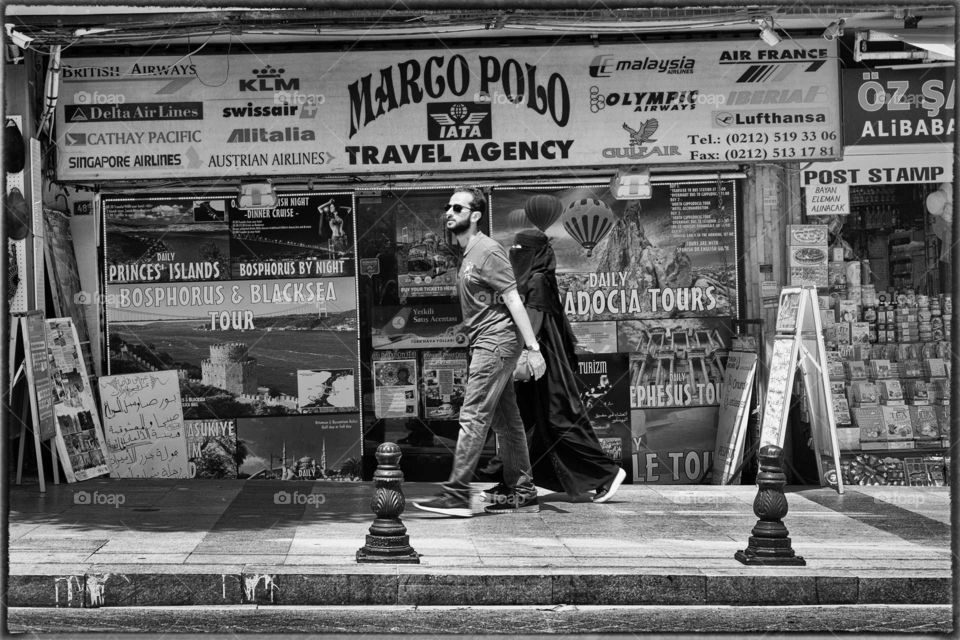 Istanbul Turkey street photography monochrome man and veiled women walking in street in front of travel agency with advertisement
