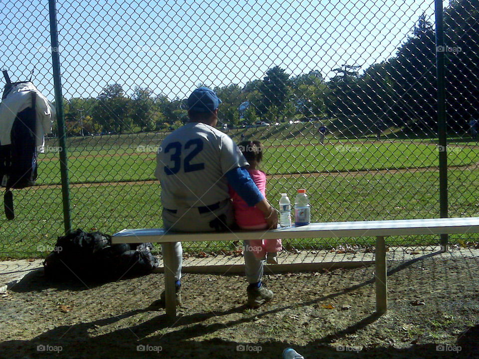 Daddy and daughter. little girl sits the bench along with her daddy at a local baseball game